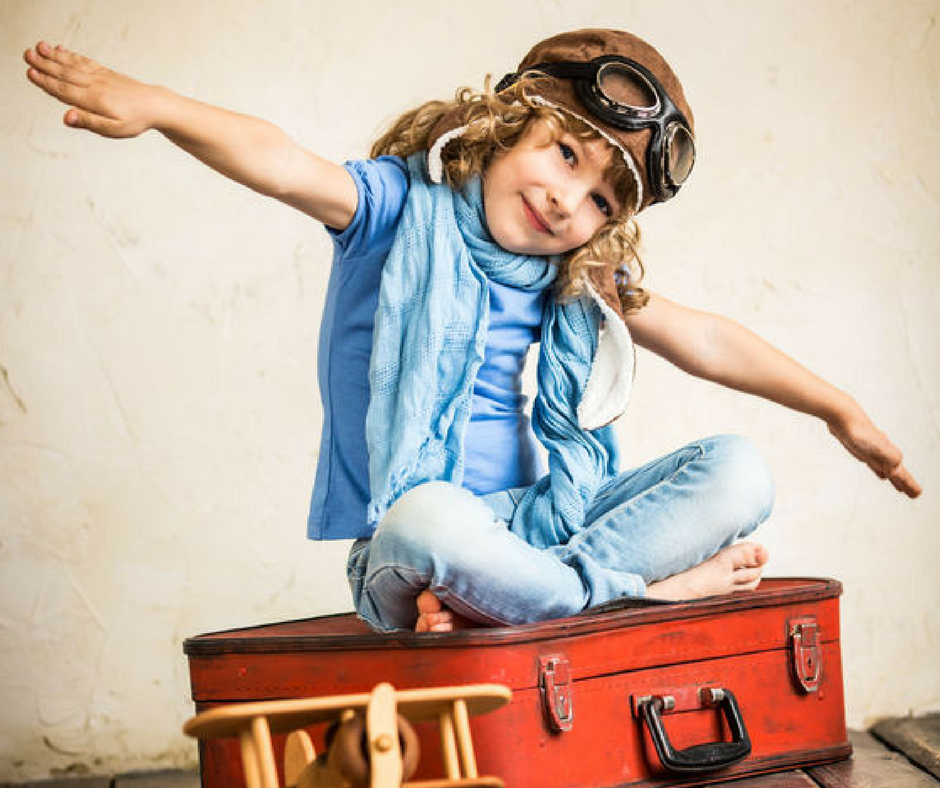 girl sitting on red suitcase pretending to fly