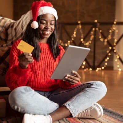 Happy black lady in Santa hat using digital tablet and credit card to buy Christmas gifts on web from home